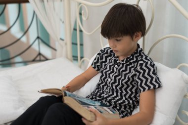 Çocuk evin içinde bir yatak üzerine bir kitap okuyor. Eğitim kavramları