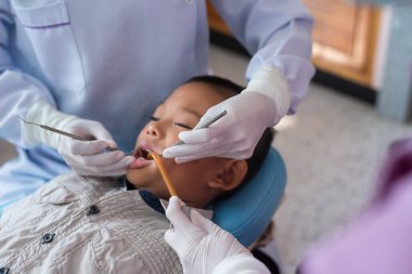 Diş hekiminin elleri diş aletini tutuyor. Hastanedeki dişçi koltuğunda yatan çocuğun dişlerini kontrol ediyorum..