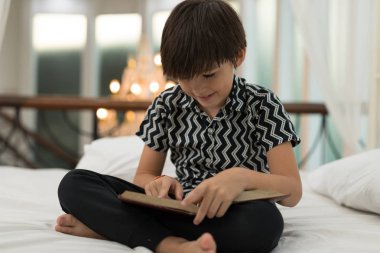 Çocuk evin içinde bir yatak üzerine bir kitap okuyor. Eğitim kavramları