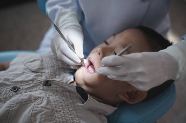 Diş hekiminin elleri diş aletini tutuyor. Hastanedeki dişçi koltuğunda yatan çocuğun dişlerini kontrol ediyorum..