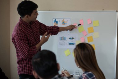 Odanın önünde dikilen sıradan ekose gömlekli genç Asyalı erkekler, konferansta başarılı bir iş yürütme konusunda meslektaşlarından geri bildirim istiyor. Takım çalışması iş toplantısı