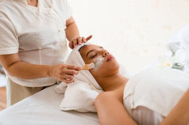 Cilt bakımı yapan bir kadın terapist. Kaplıca salonundaki yatakta yatan Asyalı bir kadınla cilde nem ekle..