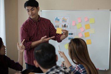 Odanın önünde dikilen sıradan ekose gömlekli genç Asyalı erkekler, konferansta başarılı bir iş yürütme konusunda meslektaşlarından geri bildirim istiyor. Takım çalışması iş toplantısı