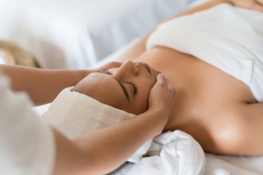 Güzel Asyalı kız güzellik salonunda yüz masajı yaptırıyor.