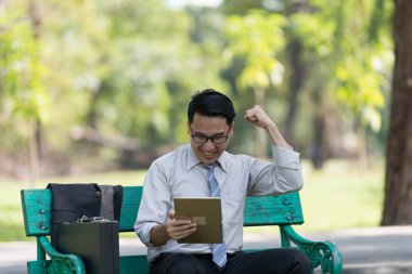 Genç işadamı parkta dijital tablet bakarak. Onların başarısı sevinç belirtileri gösteriyor. Başarılı işadamı kavramı