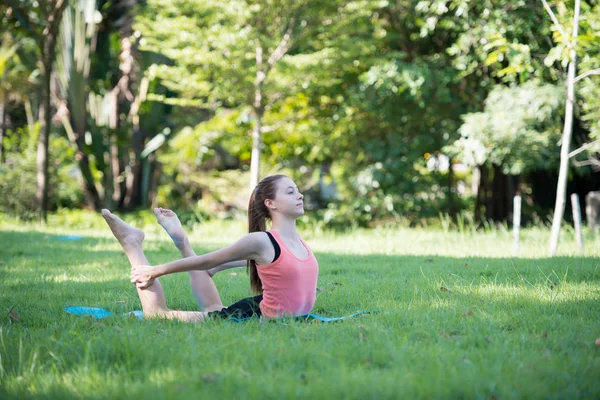 Parkta yoga yapan genç bir kadın. Sağlıklı yaşam tarzı ve rahatlama kavramı.