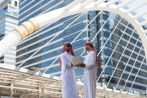 İki genç Arap işadamı, Bangkok şehrinin arka planında dizüstü bilgisayarla çalışırken konuşuyorlardı.