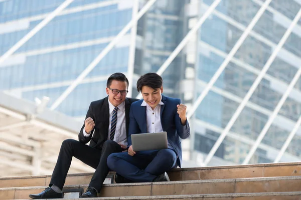 Asyalı iki işadamı dizüstü bilgisayarı izlerken mutlu oluyor. iş bölgesi arka planında