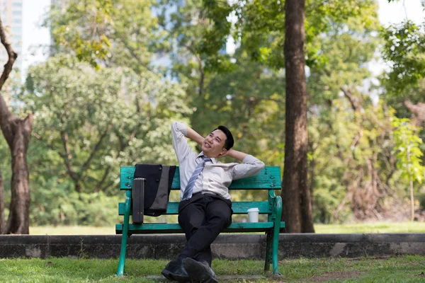 Asyalı iş adamı işten sonra parkta dinleniyor. Güneşli bir günde ağacın gölgesinin tadını çıkarıyorum. İş adamı rahatlatma, dinlenme zamanı kavramı