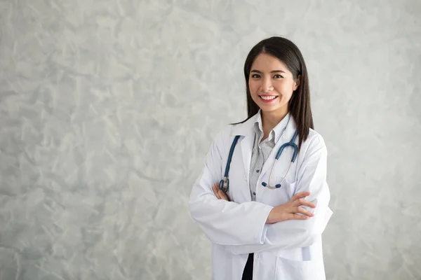 Güzel genç Asyalı Doktor ayakta çapraz kol ve stetoskop ile gülümseyen