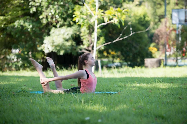 Parkta yoga yapan genç bir kadın. Sağlıklı yaşam tarzı ve rahatlama kavramı.