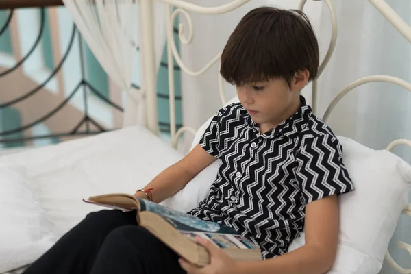 Çocuk evin içinde bir yatak üzerine bir kitap okuyor. Eğitim kavramları
