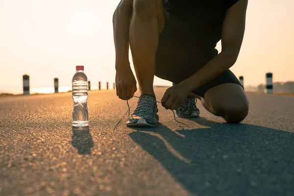 Erkek koşucu sabah ve şişe suda bir çalışma için hazırlık Ayakkabı bağlama. Sağlık ve fitness kavramı