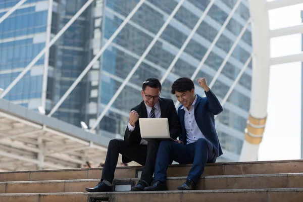 Asyalı iki işadamı dizüstü bilgisayarı izlerken mutlu oluyor. iş bölgesi arka planında