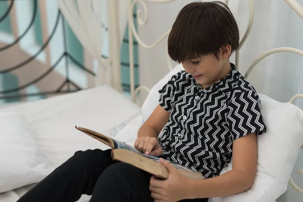 The boy is reading a book on a bed inside the house. Education Concepts