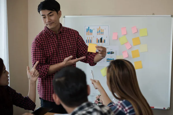 Odanın önünde dikilen sıradan ekose gömlekli genç Asyalı erkekler, konferansta başarılı bir iş yürütme konusunda meslektaşlarından geri bildirim istiyor. Takım çalışması iş toplantısı