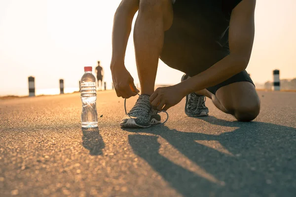 Erkek koşucu sabah ve şişe suda bir çalışma için hazırlık Ayakkabı bağlama. Sağlık ve fitness kavramı