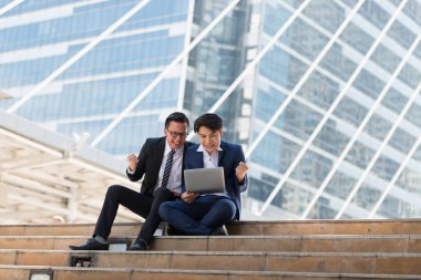 Asyalı iki işadamı dizüstü bilgisayarı izlerken mutlu oluyor. iş bölgesi arka planında