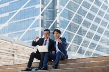 Asyalı iki işadamı dizüstü bilgisayarı izlerken mutlu oluyor. iş bölgesi arka planında