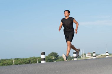 Asya genç adam gündoğumu dönemde baraj yolu egzersiz üzerinde çalıştırmak için. Sağlıklı yaşam tarzı