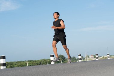 Asya genç adam gündoğumu dönemde baraj yolu egzersiz üzerinde çalıştırmak için. Sağlıklı yaşam tarzı