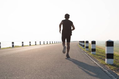 Asya genç adam gündoğumu dönemde baraj yolu egzersiz üzerinde çalıştırmak için. Sağlıklı yaşam tarzı
