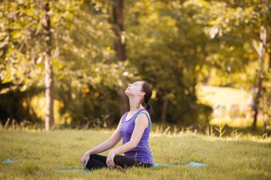Parkta yoga yapan genç bir kadın. Sağlıklı yaşam tarzı ve rahatlama kavramı.