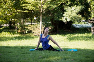 Pratik yoga açık parkta gülümseme bir genç kadın. Sağlıklı yaşam tarzı ve gevşeme kavramı.