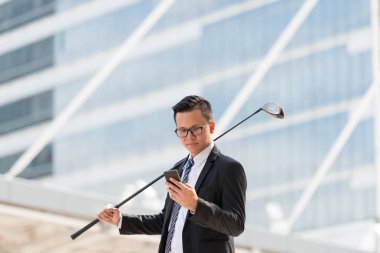 Takım elbiseli başarılı bir iş adamı. Şehri ayakta tutan golf ekipmanları ve akıllı telefonlar. Şehir arka planında başarı kavramı