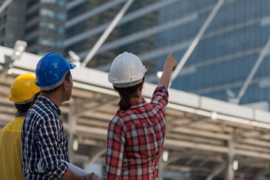 Asya mühendisleri grup planı kağıt basılı tutarak çalışma sitesi yapı inşaat bakın. Şehir arka planda. ekip çalışması kavramı