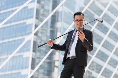 Takım elbiseli başarılı bir iş adamı. Şehri ayakta tutan golf ekipmanları ve akıllı telefonlar. Şehir arka planında başarı kavramı