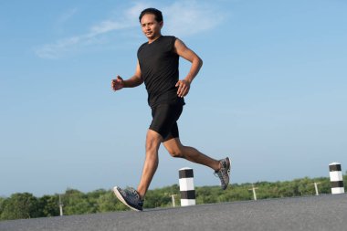Asya genç adam gündoğumu dönemde baraj yolu egzersiz üzerinde çalıştırmak için. Sağlıklı yaşam tarzı
