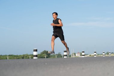 Asya genç adam gündoğumu dönemde baraj yolu egzersiz üzerinde çalıştırmak için. Sağlıklı yaşam tarzı