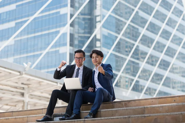 Asyalı iki işadamı dizüstü bilgisayarı izlerken mutlu oluyor. iş bölgesi arka planında