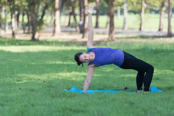 Parkta yoga yapan genç bir kadın. Sağlıklı yaşam tarzı ve rahatlama kavramı.