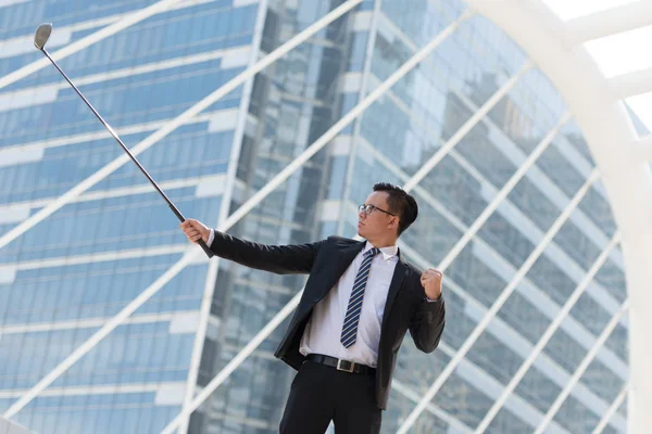 Takım elbiseli başarılı bir iş adamı. golf ekipmanları kentin ayakta tutan el. Şehir arka plan başarı kavramı