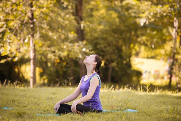 Parkta yoga yapan genç bir kadın. Sağlıklı yaşam tarzı ve rahatlama kavramı.