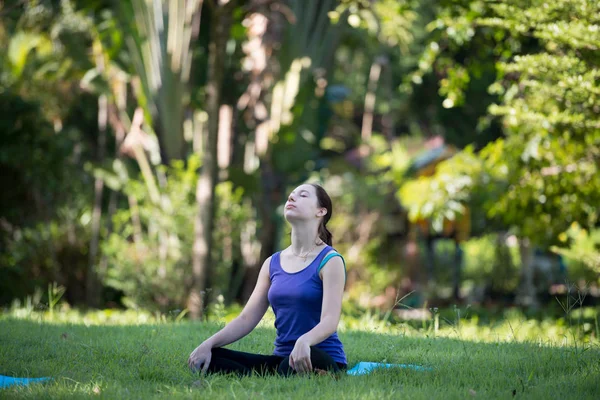 Parkta yoga yapan genç bir kadın. Sağlıklı yaşam tarzı ve rahatlama kavramı.