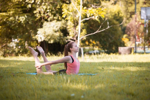 Parkta yoga yapan genç bir kadın. Sağlıklı yaşam tarzı ve rahatlama kavramı.