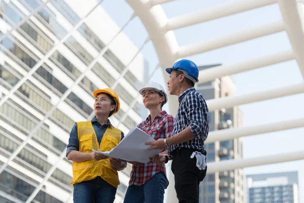 Asya mühendisleri grup planı kağıt basılı tutarak çalışma sitesi yapı inşaat bakın. Şehir arka planda. ekip çalışması kavramı
