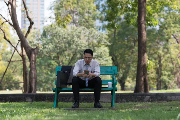 Business man sit check email on  mobile phone at the Park  on the way back home.