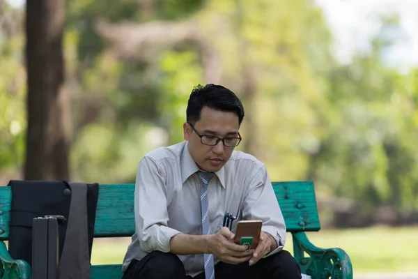 Business man sit check email on  mobile phone at the Park  on the way back home.