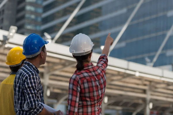 Asya mühendisleri grup planı kağıt basılı tutarak çalışma sitesi yapı inşaat bakın. Şehir arka planda. ekip çalışması kavramı