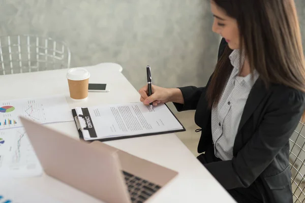 Businesswoman at work signing a contract paper in her workstation. Business agreement concept