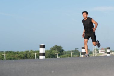 Asya genç adam gündoğumu dönemde baraj yolu egzersiz üzerinde çalıştırmak için. Sağlıklı yaşam tarzı