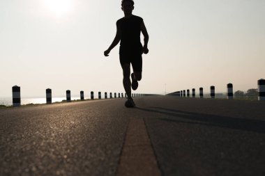 Gündoğumu sırasında verilen sürede baraj yolu üzerinde çalışan bir adam Asya bacaklar görünümünü aşağı egzersiz. Sağlıklı yaşam tarzı