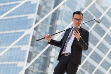 Takım elbiseli başarılı bir iş adamı. Şehri ayakta tutan golf ekipmanları ve akıllı telefonlar. Şehir arka planında başarı kavramı