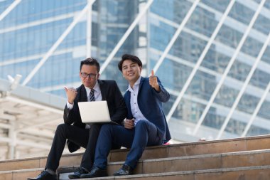 Asyalı iki işadamı dizüstü bilgisayarı izlerken mutlu oluyor. iş bölgesi arka planında