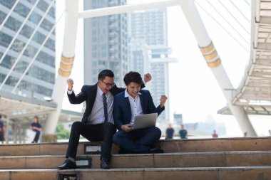 Asyalı iki işadamı dizüstü bilgisayarı izlerken mutlu oluyor. iş bölgesi arka planında