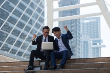 Asyalı iki işadamı dizüstü bilgisayarı izlerken mutlu oluyor. iş bölgesi arka planında